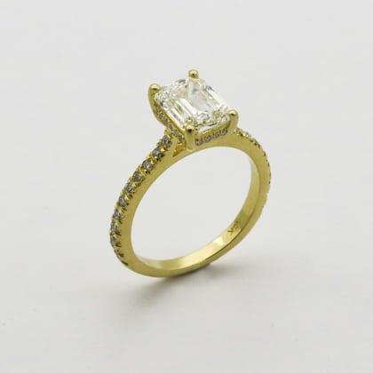 Yellow gold ring with an emerald-cut solitaire and diamond-set shoulders, on white